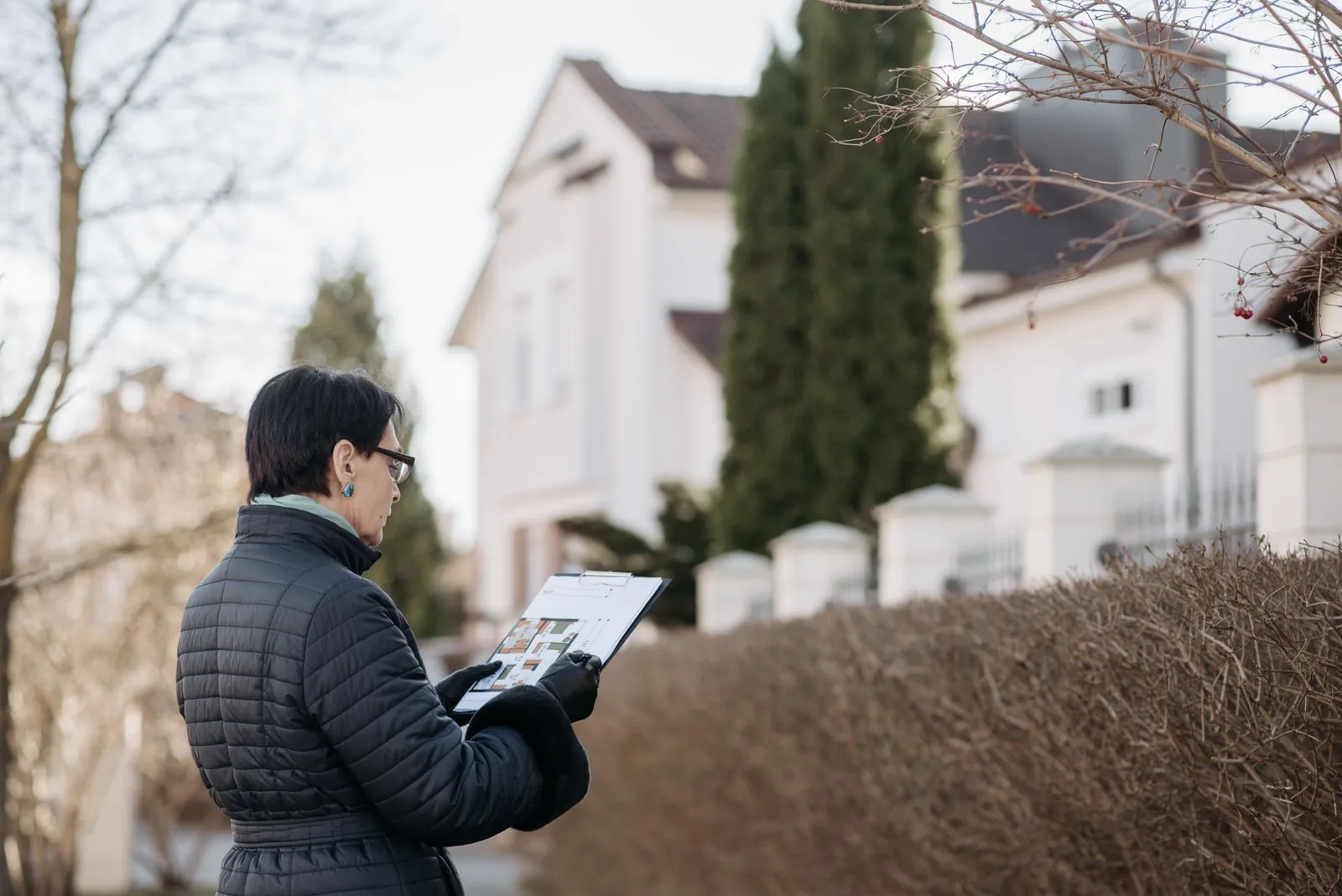 An appraiser with a clipboard looking over a house from the street